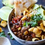 A bowl of taco truck chili with fritos and pita