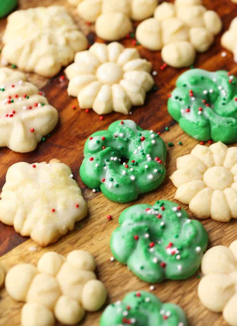 Perfect Spritz Cookies in various shapes and colors arranged on a wooden countertop.