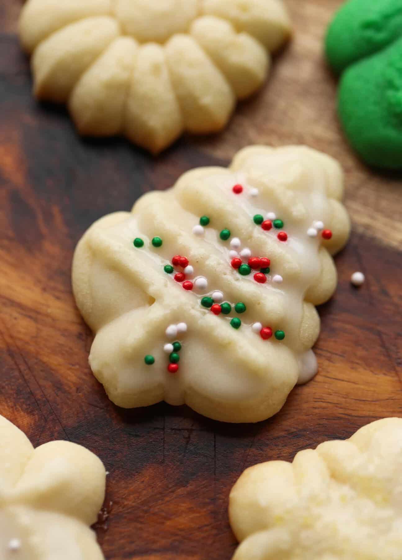 Spritz cookies with glass and sprinkles on a wooden cutting board