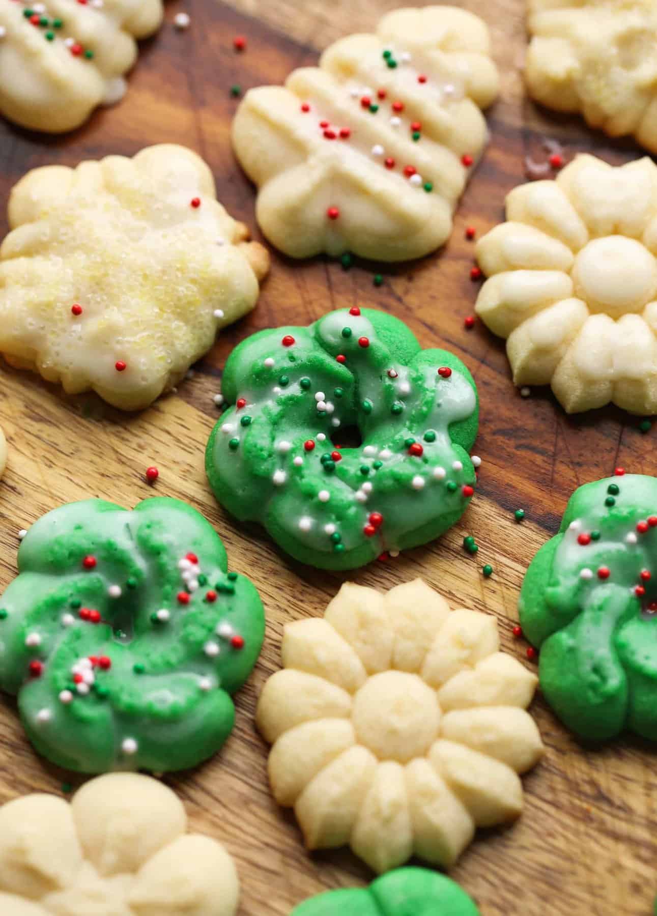 Green spritz cookies with glaze and sprinkles on a wooden surface