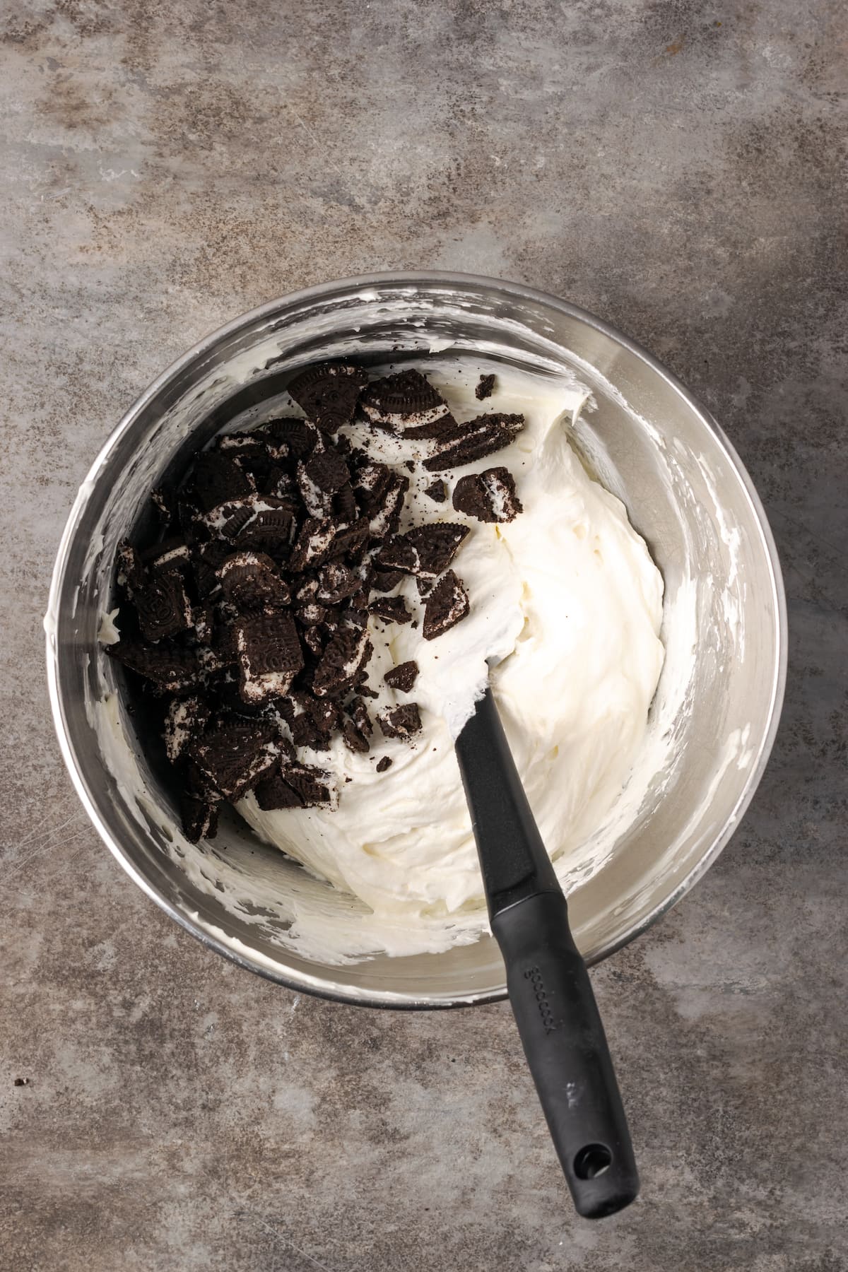 Chopped Oreo cookies added to a bowl of cream cheese frosting.