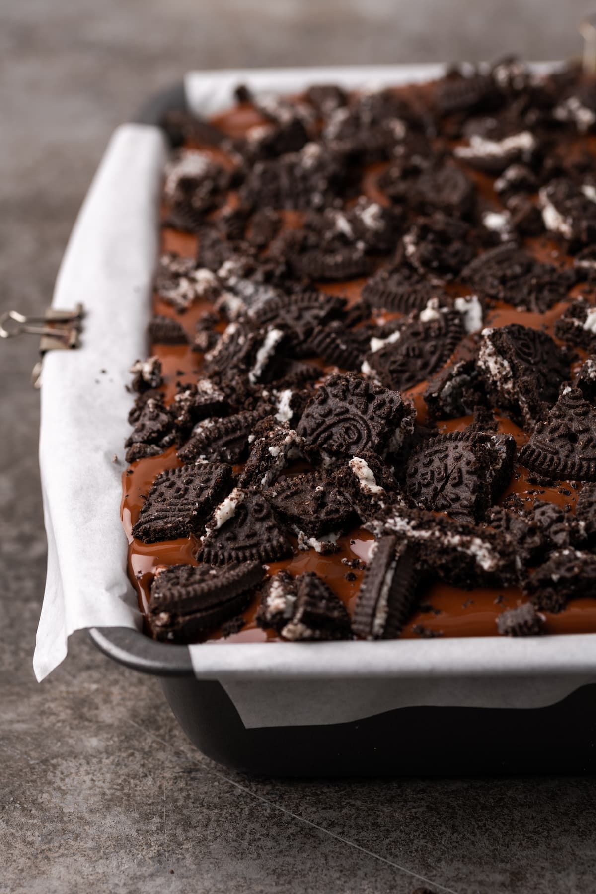 Chopped Oreo cookies are scattered over top Oreo brownies in a baking pan.