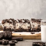 Oreo brownies on a wooden platter next to a glass of milk and chopped Oreo cookies.