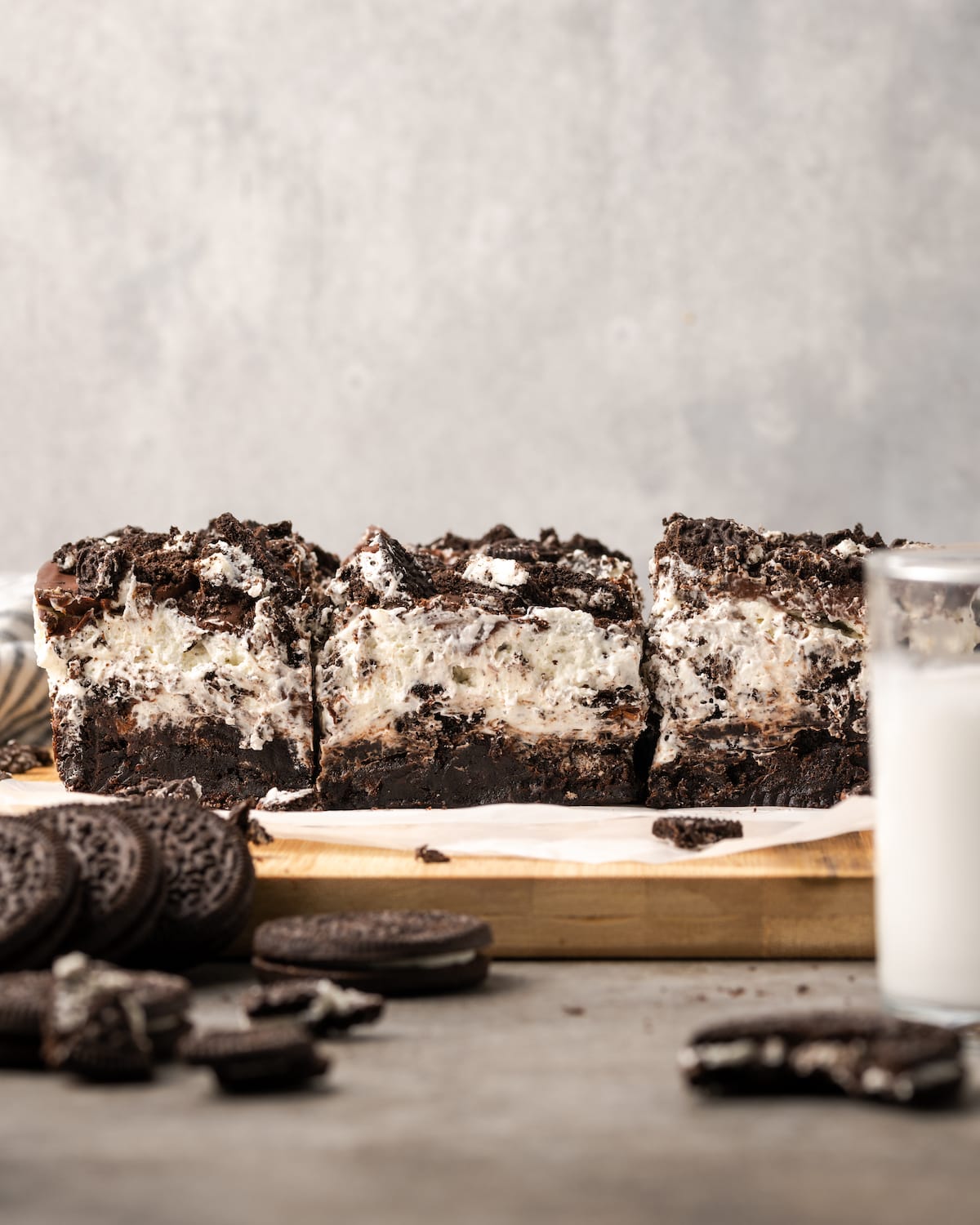 Oreo brownies on a wooden platter next to a glass of milk and chopped Oreo cookies.