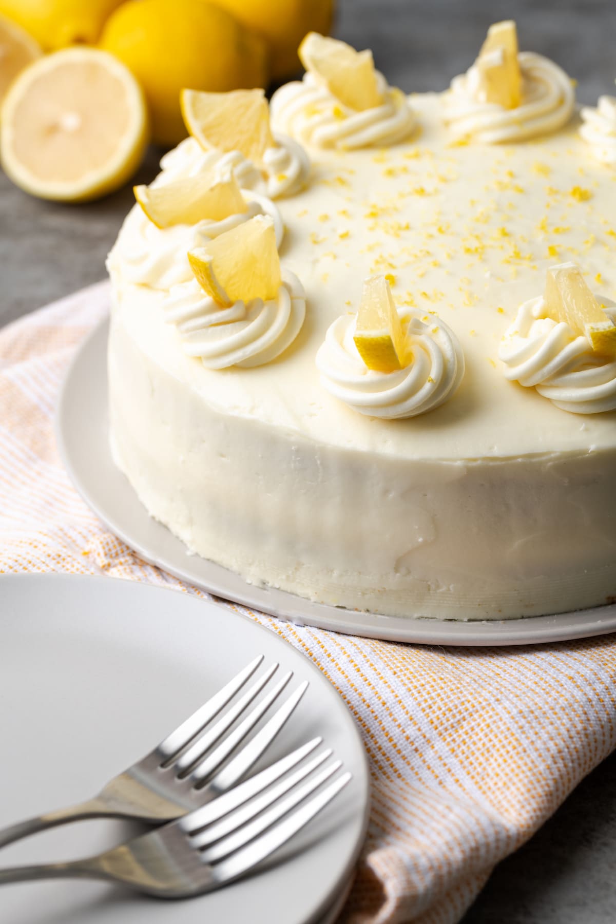 Lemonade cake topped with frosting swirls and lemon slices next to a plate with two forks.
