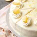 Lemonade cake topped with frosting swirls and lemon slices, with a slice cut into it.