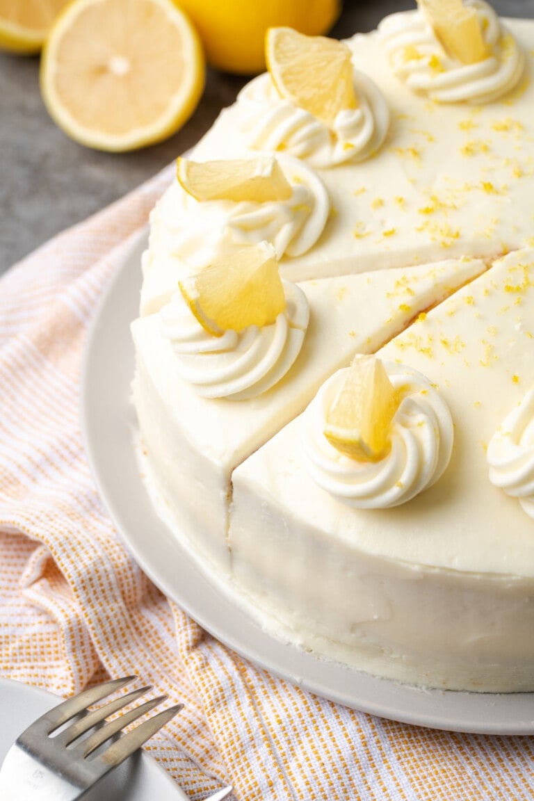 Lemonade cake topped with frosting swirls and lemon slices and cut into slices.