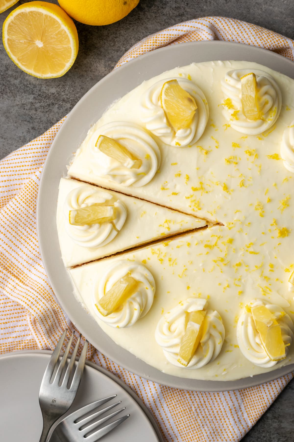 Overhead view of lemonade cake topped with frosting swirls and lemon wedges, with slice cut on it.
