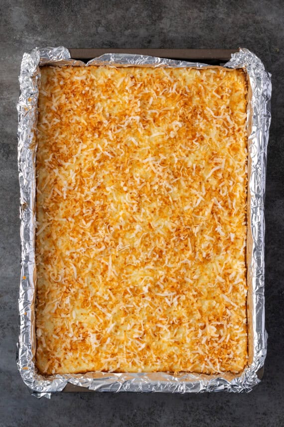 Coconut lime cheesecake bars topped with toasted coconut in a baking pan.