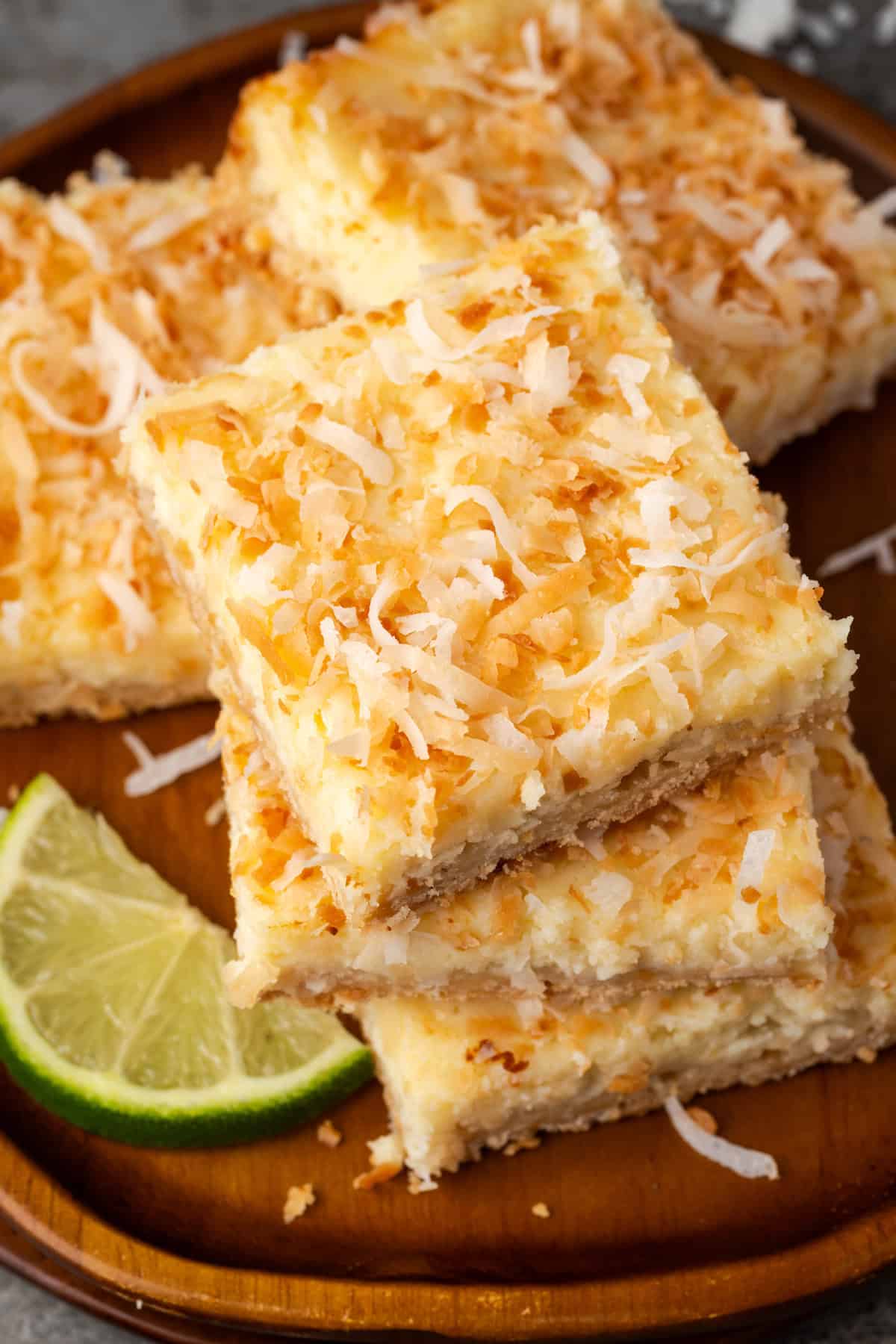 Overhead view of a stack of three coconut lime cheesecake bars on a plate, with more bars in the background.