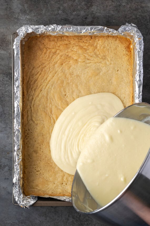 Coconut lime cheesecake batter being poured over a par-baked shortbread crust in a baking pan.
