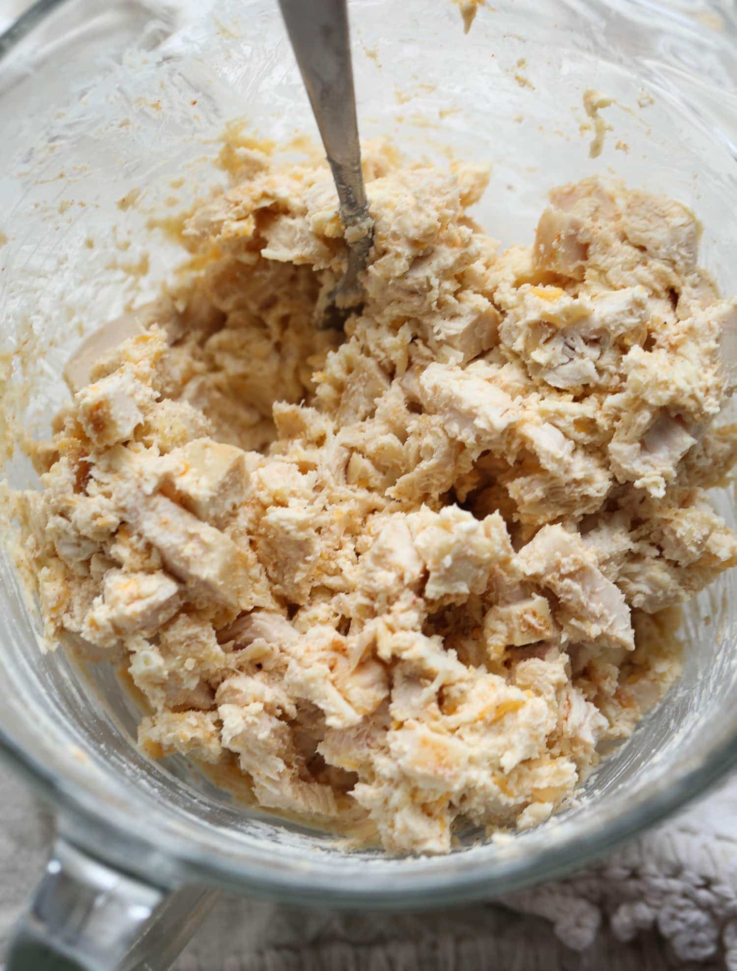 chicken, grated cheddar cheese, cream cheese, and seasonings mixed together in a glass bowl.