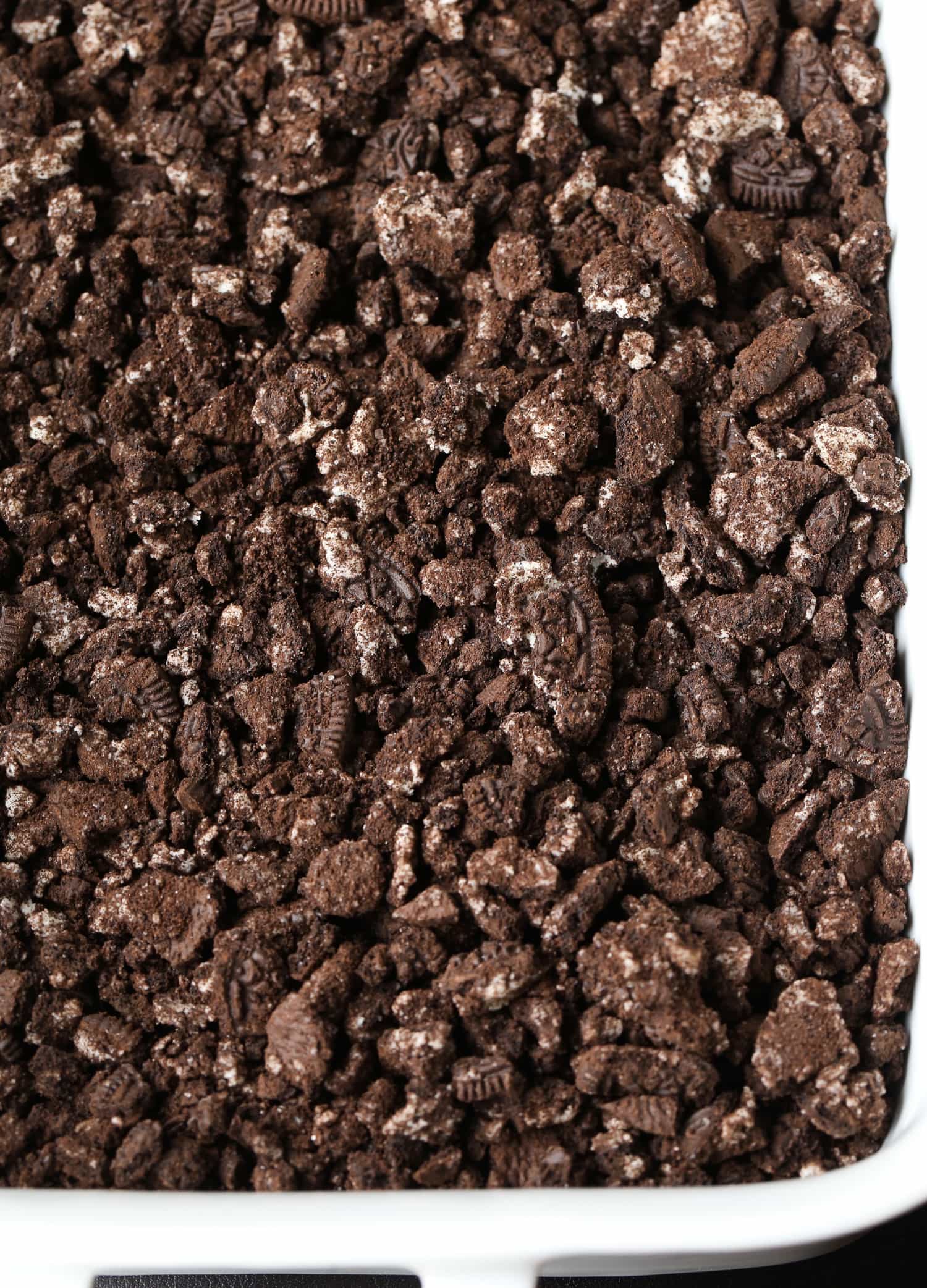 Crushed chocolate cookie crumbs are spread over top of the cream cheese cake filling.