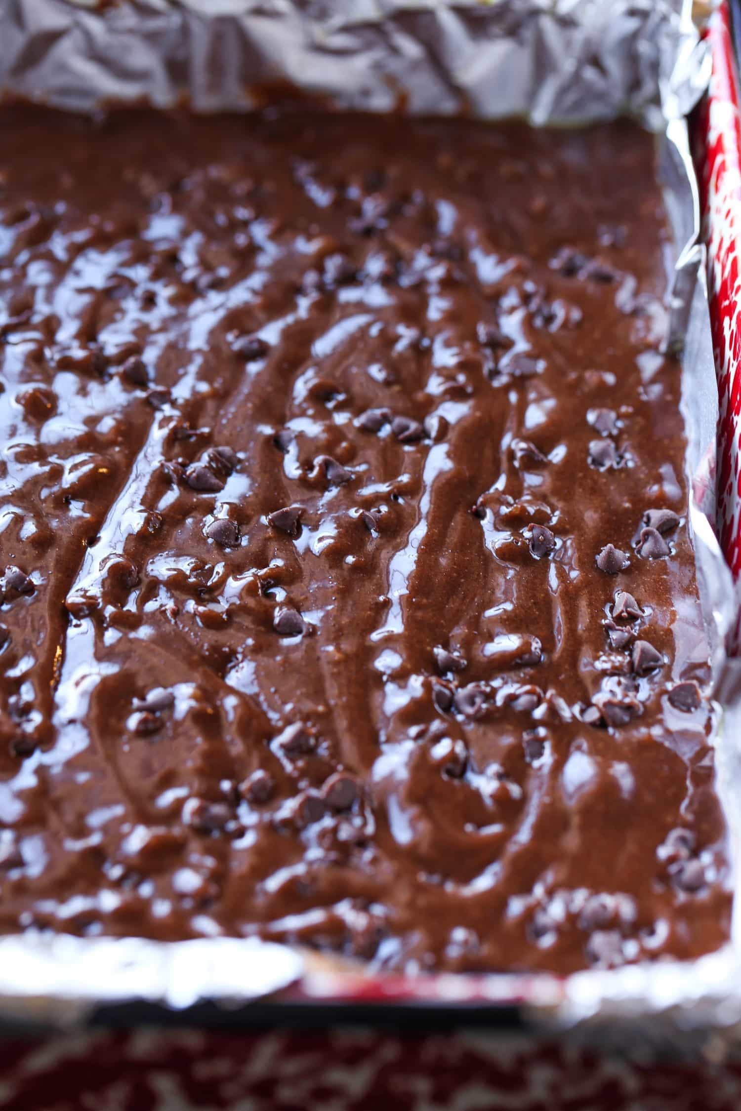 Brownie batter topped with chocolate chips in a parchment-lined baking pan.