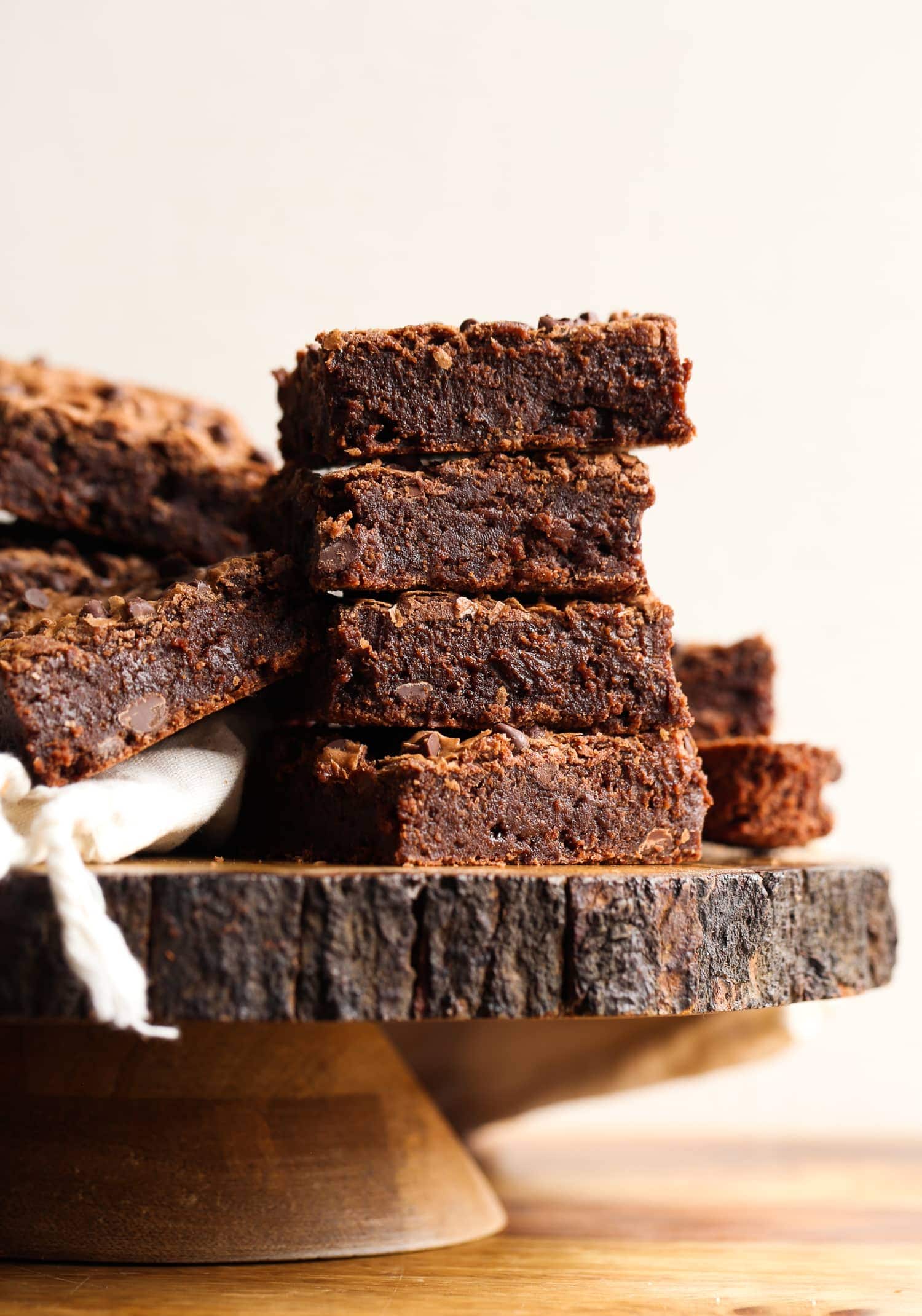 Side view of fudgy brownies stacked on top of a wooden cake stand.