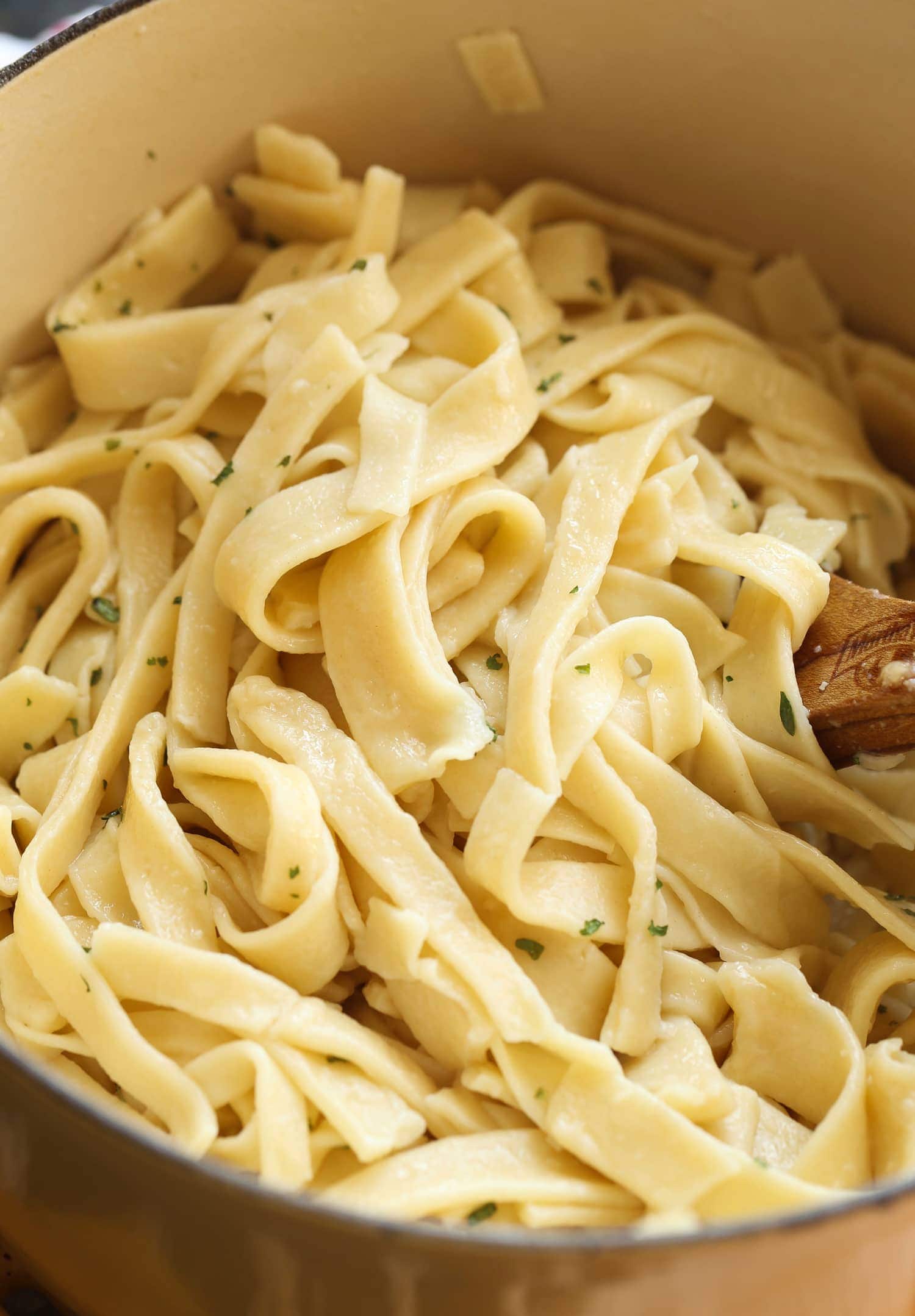 Close up of egg noodles in a pot with some parsley and a wooden spoon