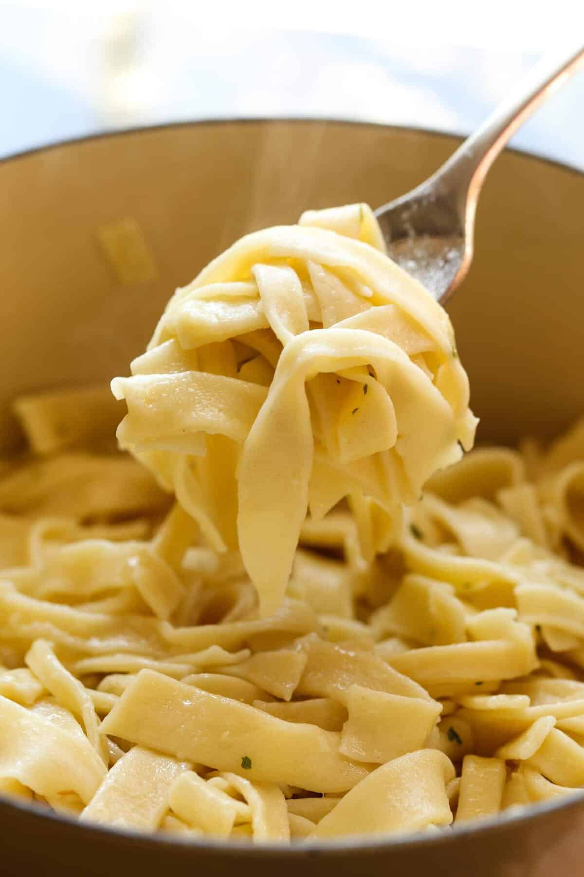 A fork lifting a forkful of egg noodles out of a pot