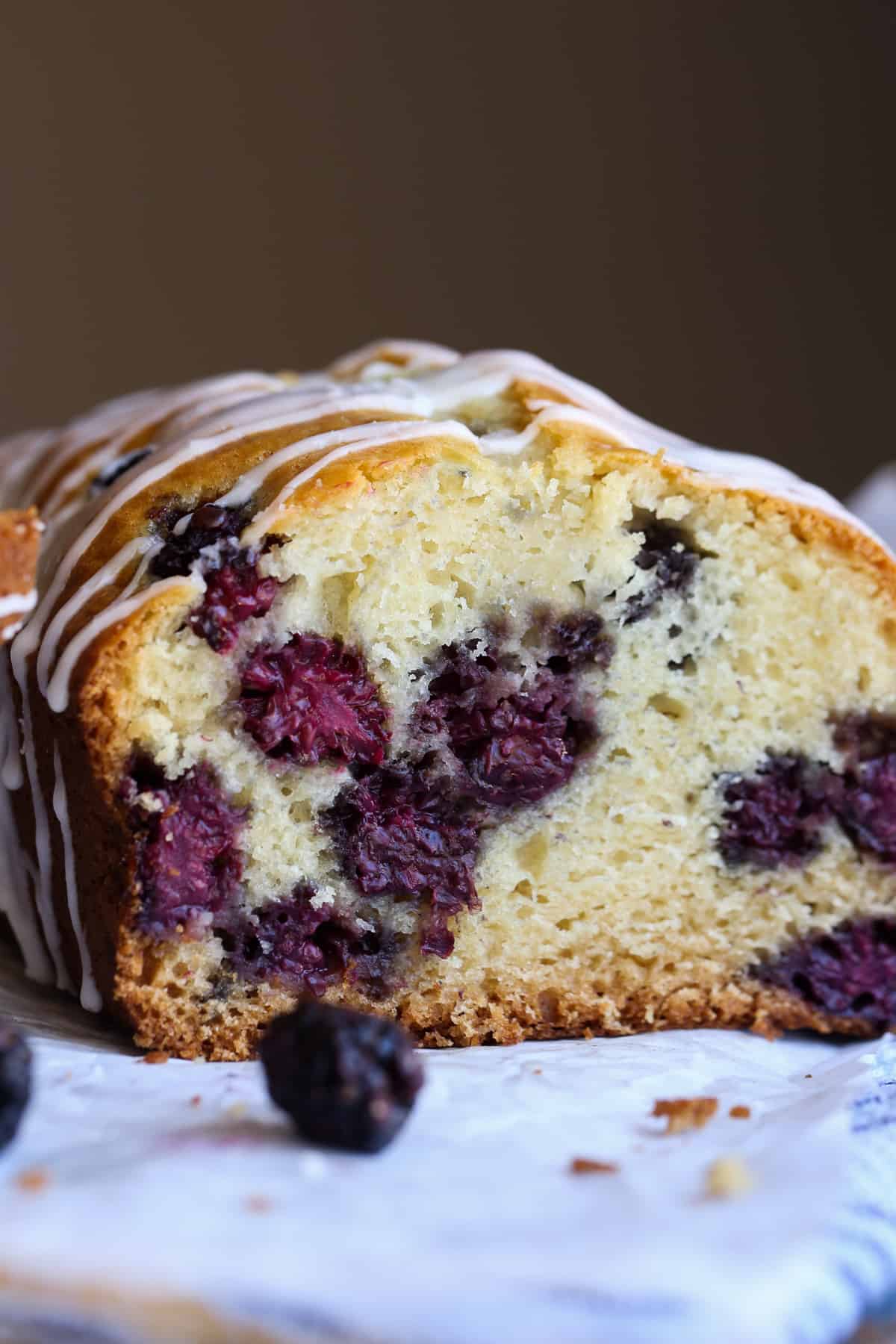 A loaf of blackberry bread sliced showing the inside of the loaf with fresh blackberries