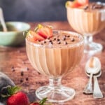 Two bowls of chocolate mousse with chocolate chips and stawberries.