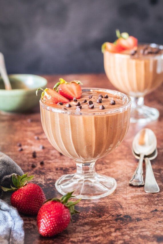 Two bowls of chocolate mousse with chocolate chips and stawberries.
