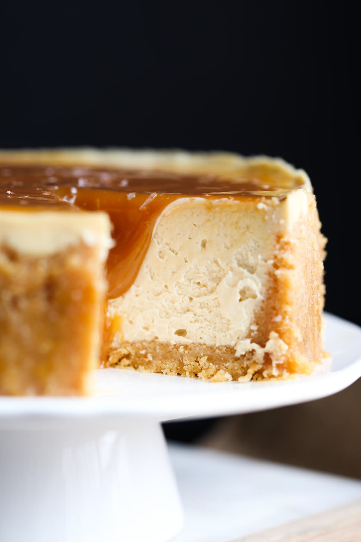 Close up of caramel Instant Pot cheesecake on a white cake stand, with a slice missing.