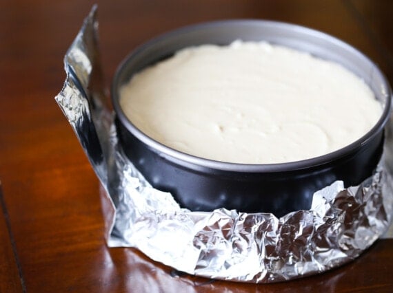Cheesecake filling in a springform pan wrapped with aluminum foil.