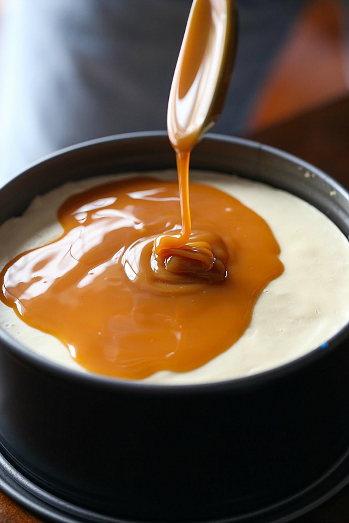 A spoon drizzles caramel sauce over top of an Instant Pot cheesecake inside a springform pan.