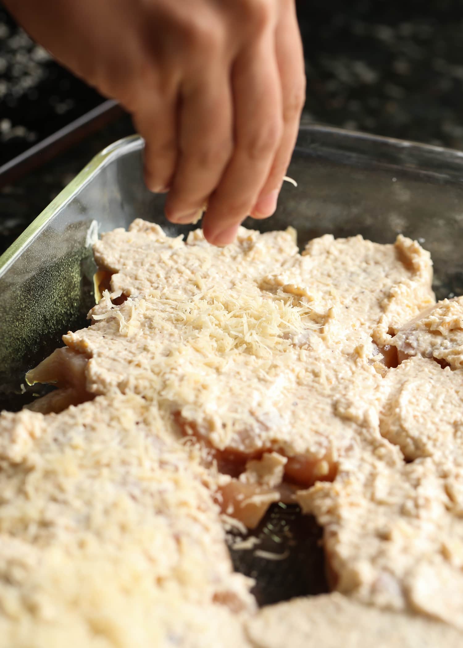 sprinkling parmesan cheese onto chicken breasts in a baking dish