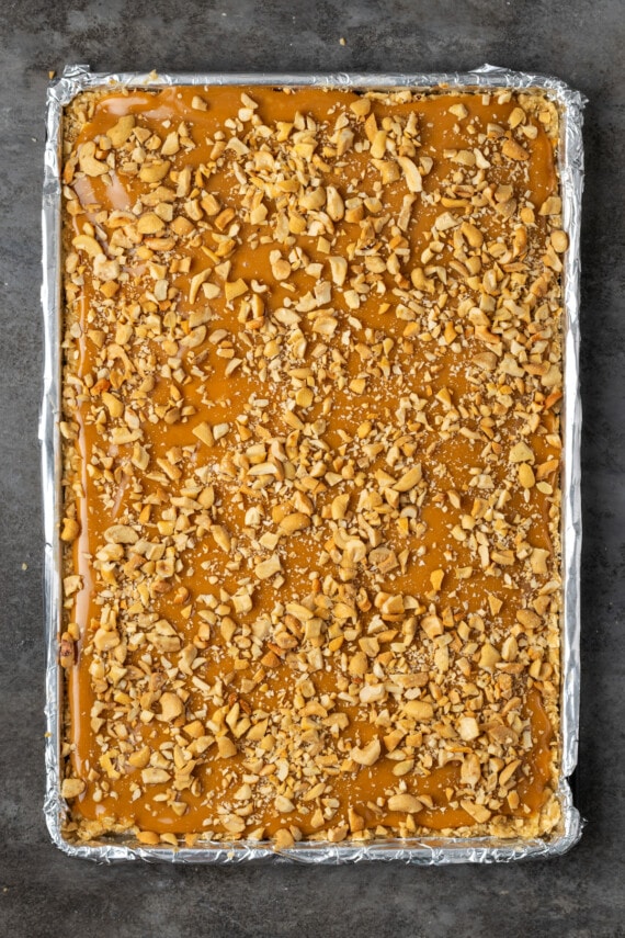 Caramel oat bars in a sheet pan topped with chopped cashews.