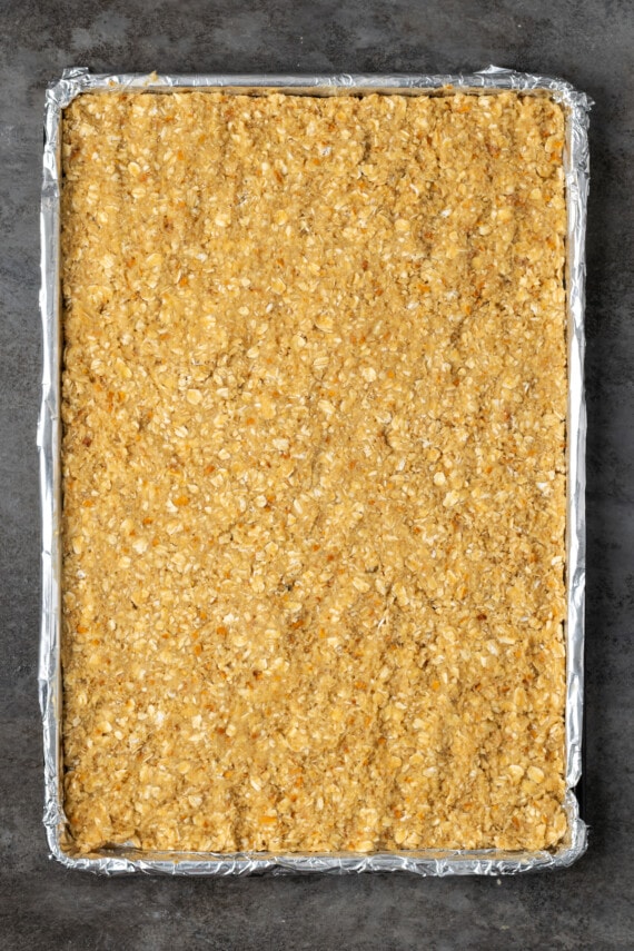 The dough for caramel oat bars pressed into a lined sheet pan.