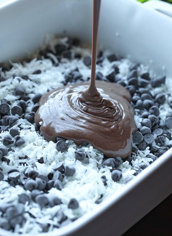 Chocolate cake batter is poured over chocolate chips and shredded coconut scattered in the bottom of a baking dish.