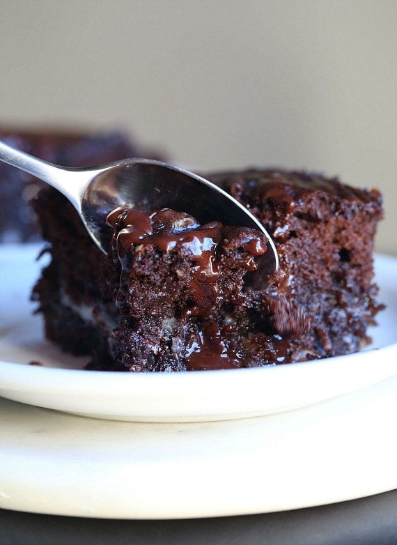 A spoon scoops a spoonful of earthquake cake from a slice on a white plate.