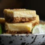 Pretzel Crusted Key Lime Bars stacked in a bowl next to a key lime wedge.