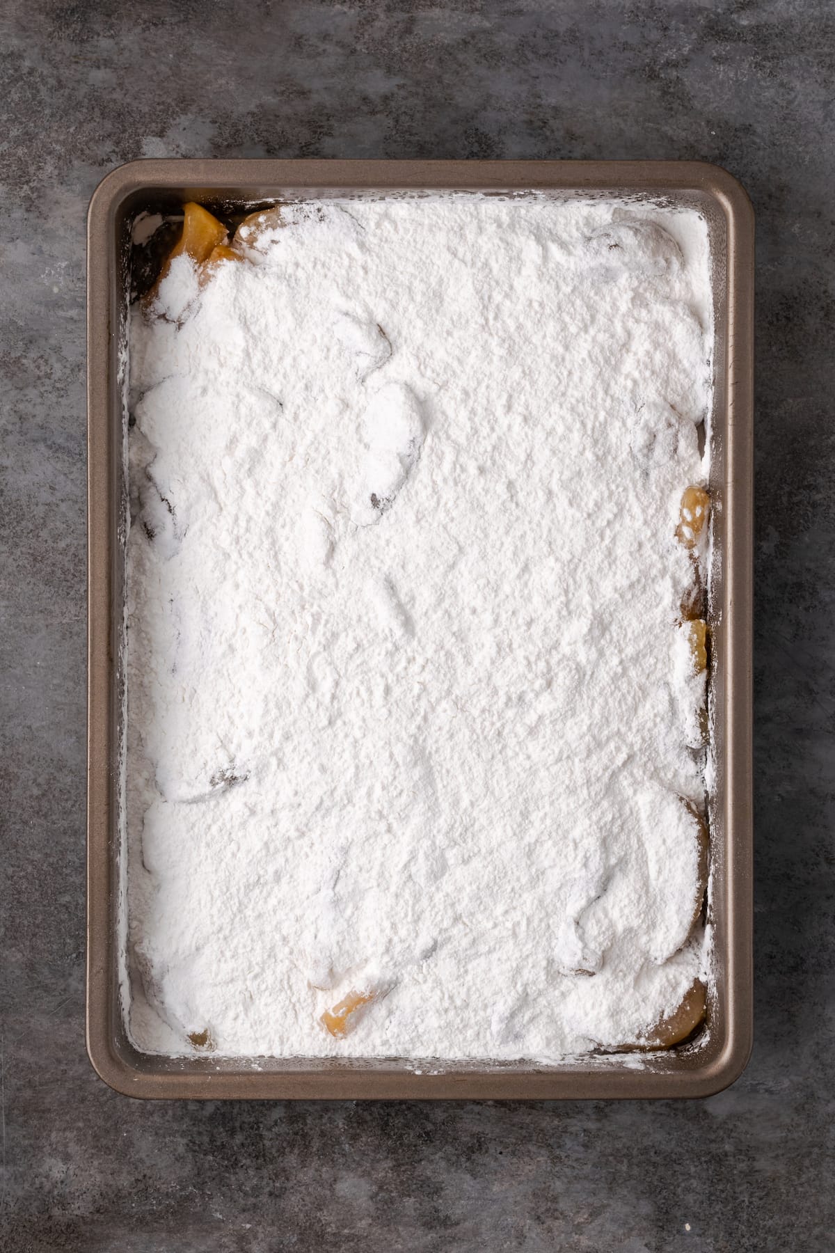 Apple pie filling topped with boxed cake mix in a baking pan.