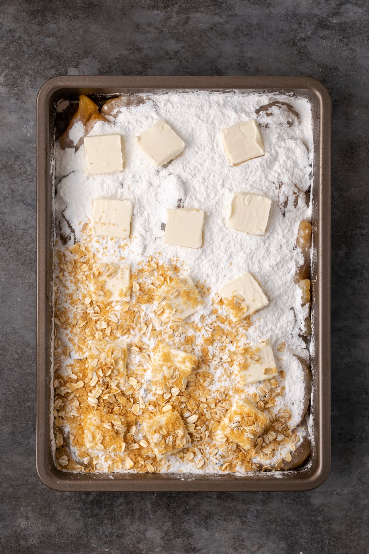 Rolled oats and butter scattered over top of dump cake ingredients in a baking pan.