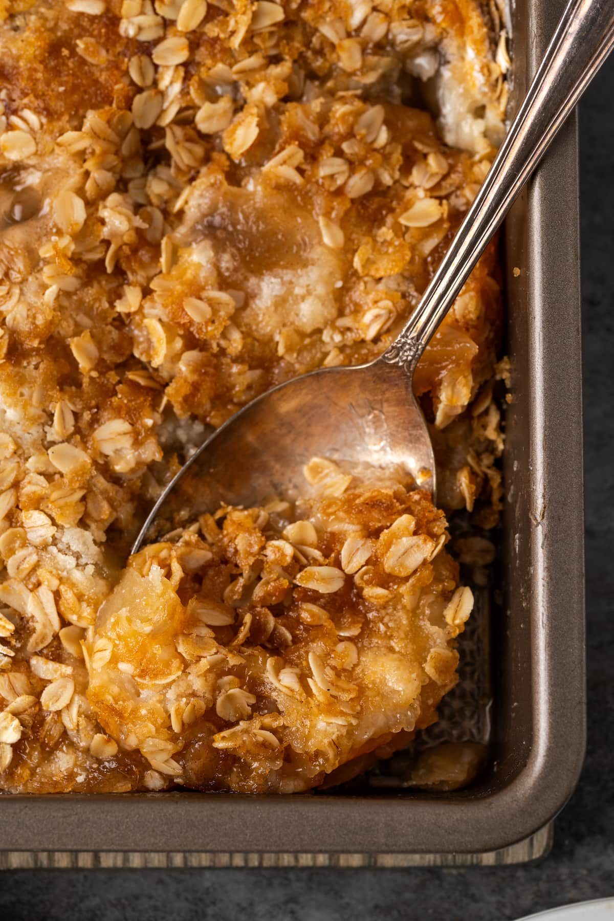 Overhead view of a spoon stuck into the corner of a baked apple dump cake in a baking pan.
