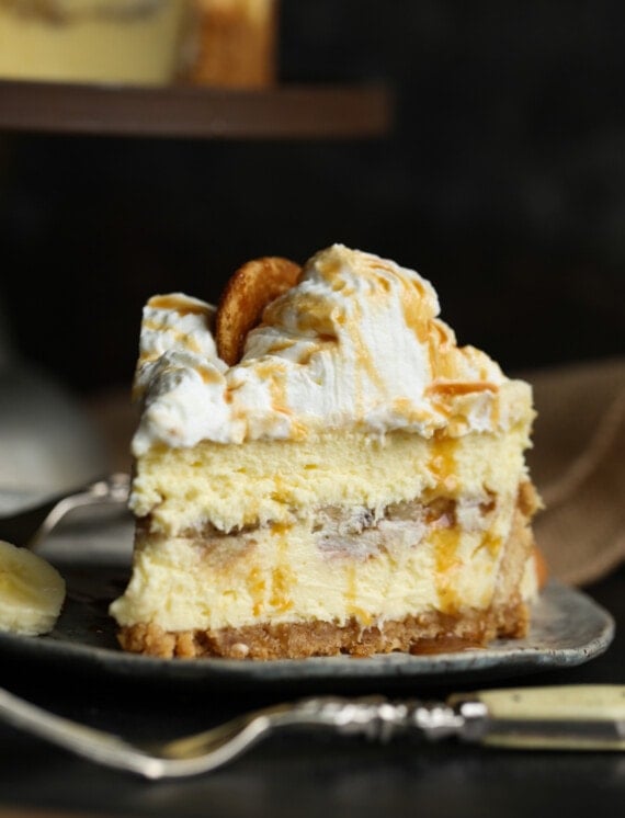 A slice of banana pudding cheesecake on a plate, with a fork in the foreground.