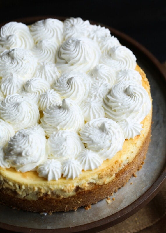 Banana pudding cheesecake topped with whipped cream on a cake stand.