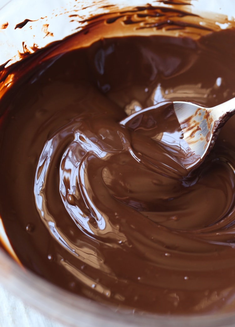 A spoon stirring melted chocolate in a mixing bowl.