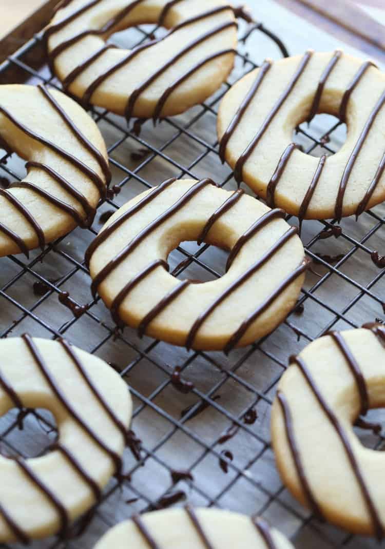 Cutout vanilla cookies drizzled with dark chocolate stripes on a wire rack.