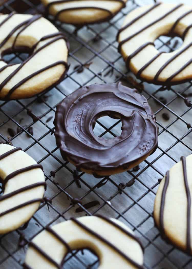 Vanilla cookies drizzled with chocolate stripes on a wire rack, with one cookie flipped over with the bottom dipped in chocolate.