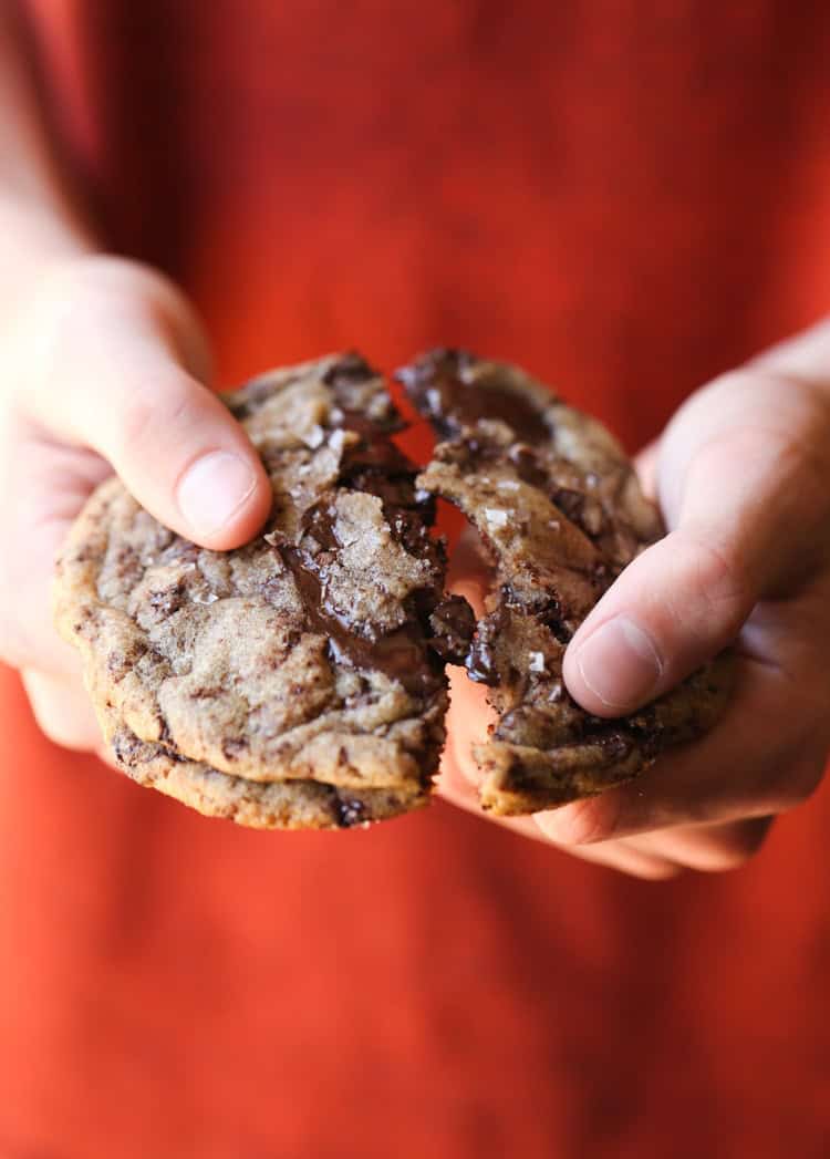 Hands breaking a chocolate chip cookie in half.