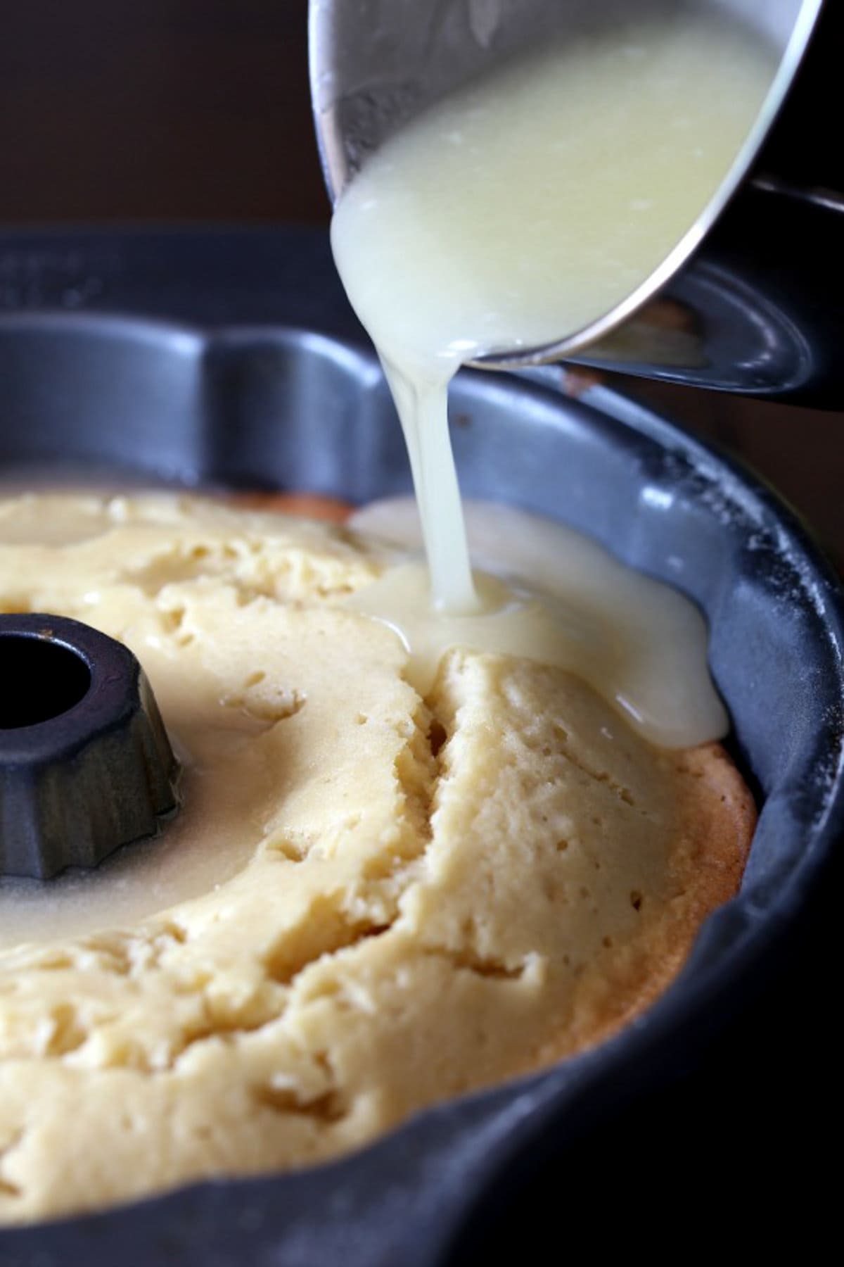 Pouring sugar syrup on top of a baked butter cake in a bundt pan