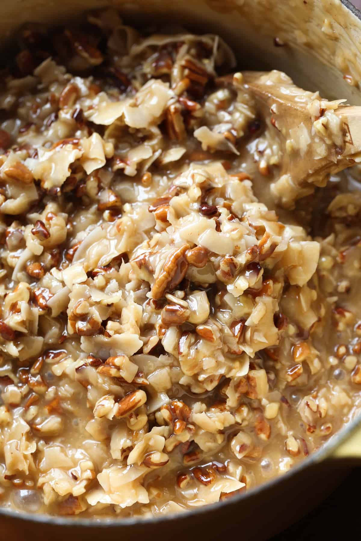 A mixture of coconut, pecans, and warm brown sugar candy mixture in a bowl stirred together.