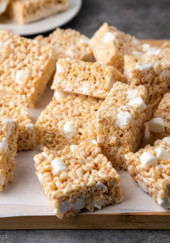 Assorted Rice Krispie Treats on a wooden platter lined with parchment paper.