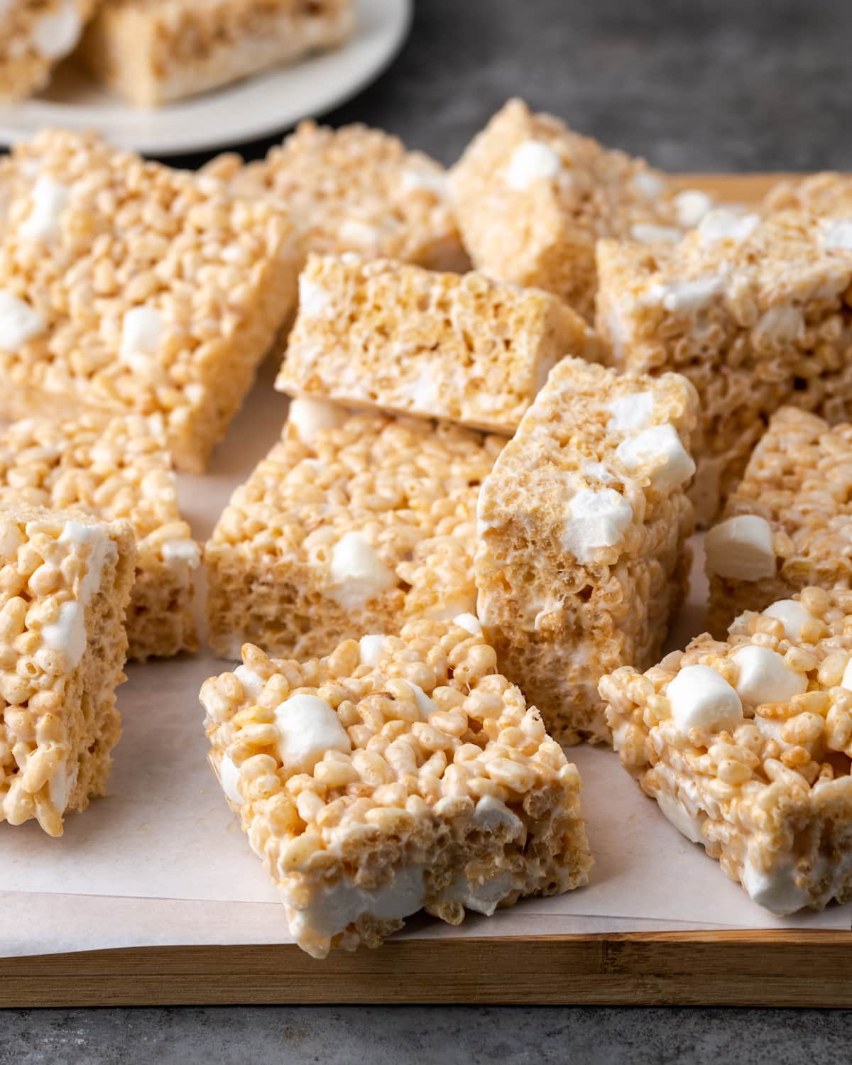 Assorted Rice Krispie Treats on a wooden platter lined with parchment paper.