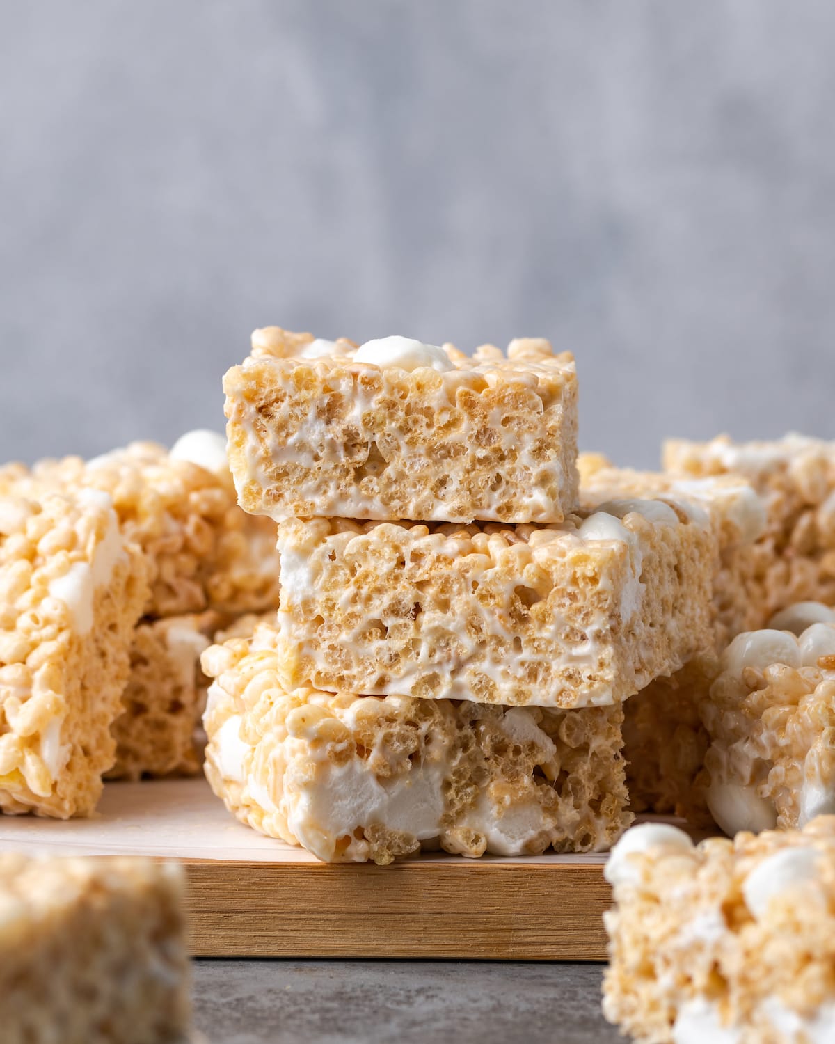 Rice Krispie Treats stacked on a wooden platter lined with parchment paper.