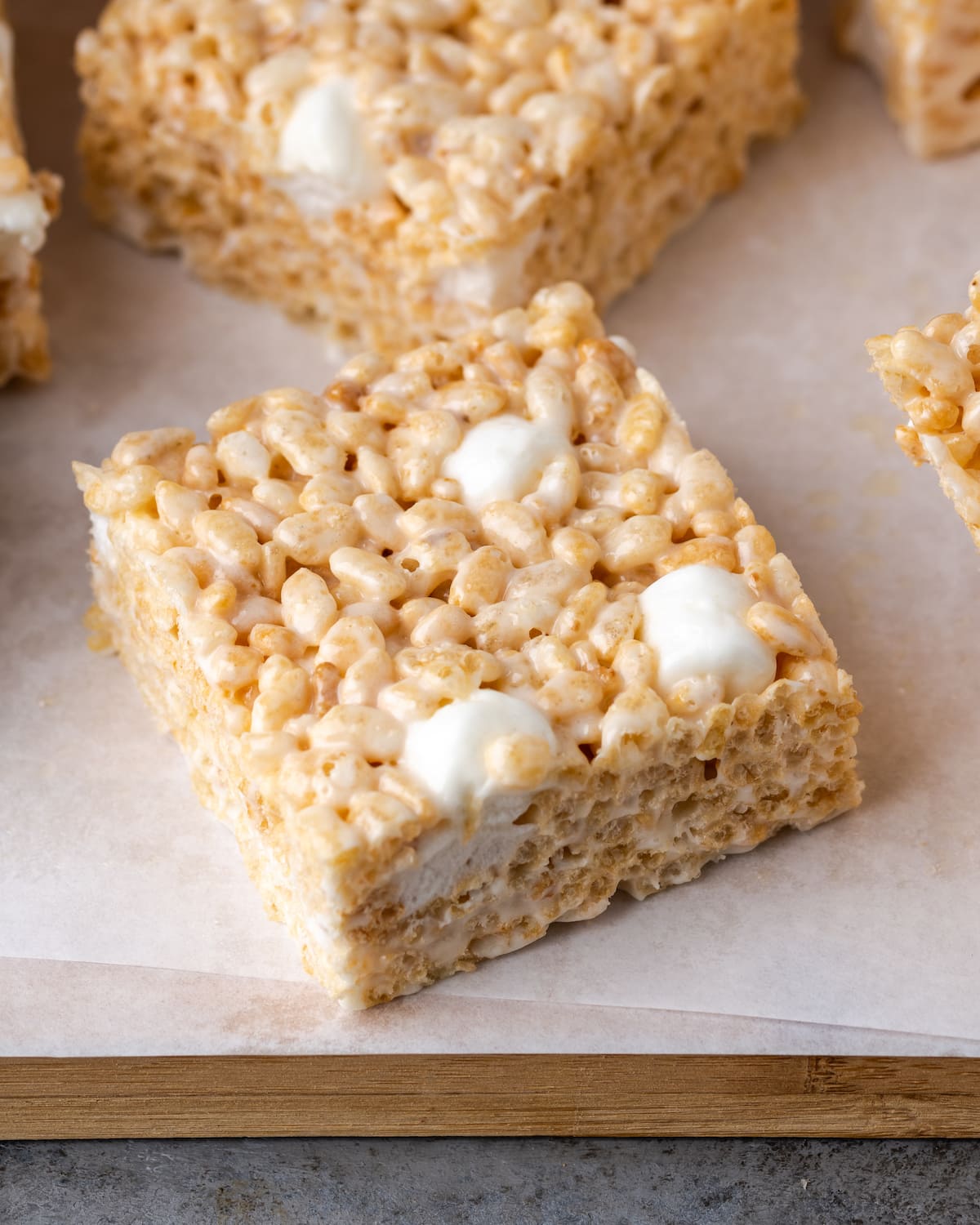 Close up of a Rice Krispie Treat on a wooden platter lined with parchment paper.