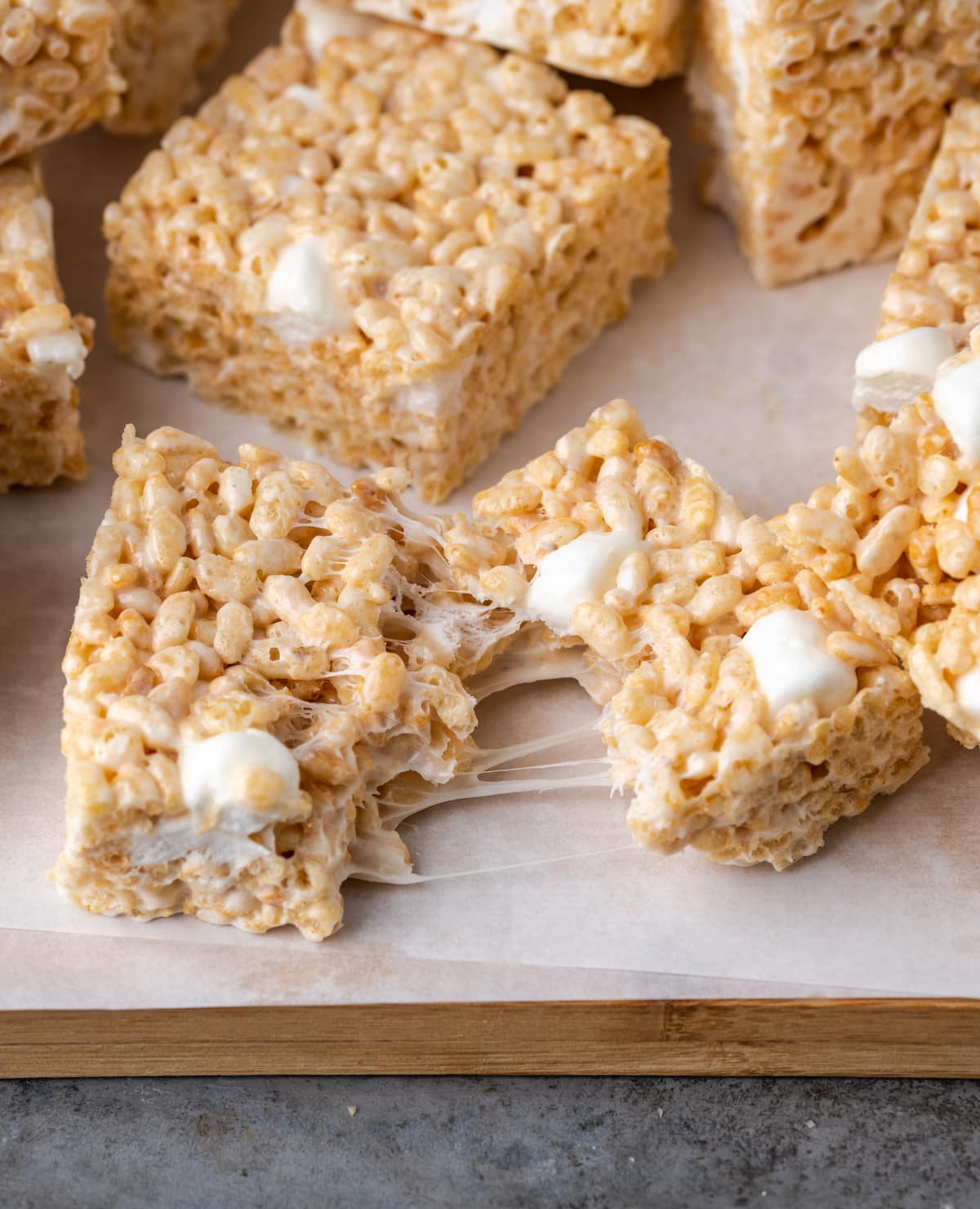 A Perfect Rice Krispie Treat pulled in two, on a wooden platter lined with parchment paper.