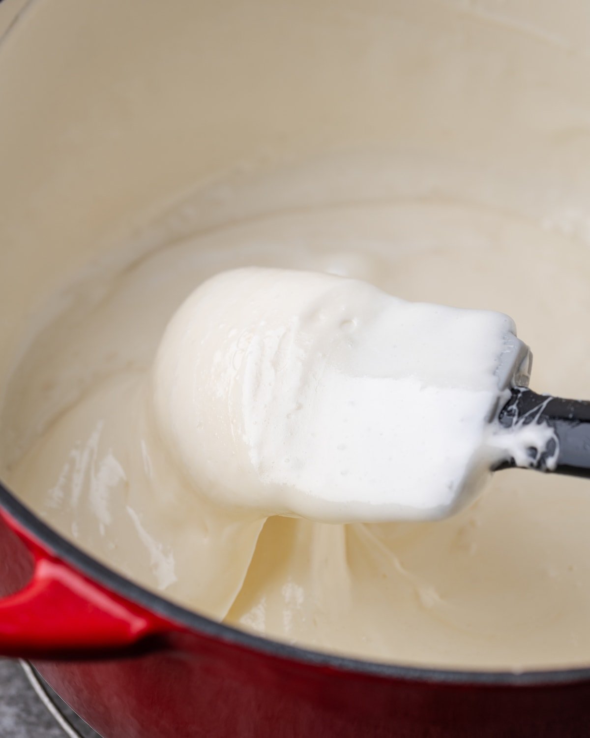 A spatula stirs the melted marshmallow and butter mixture in a red pot.